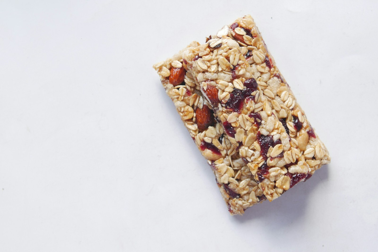Một thanh granola với oats, hạt và berry khô, nằm đơn lẻ trên nền sáng minimal.