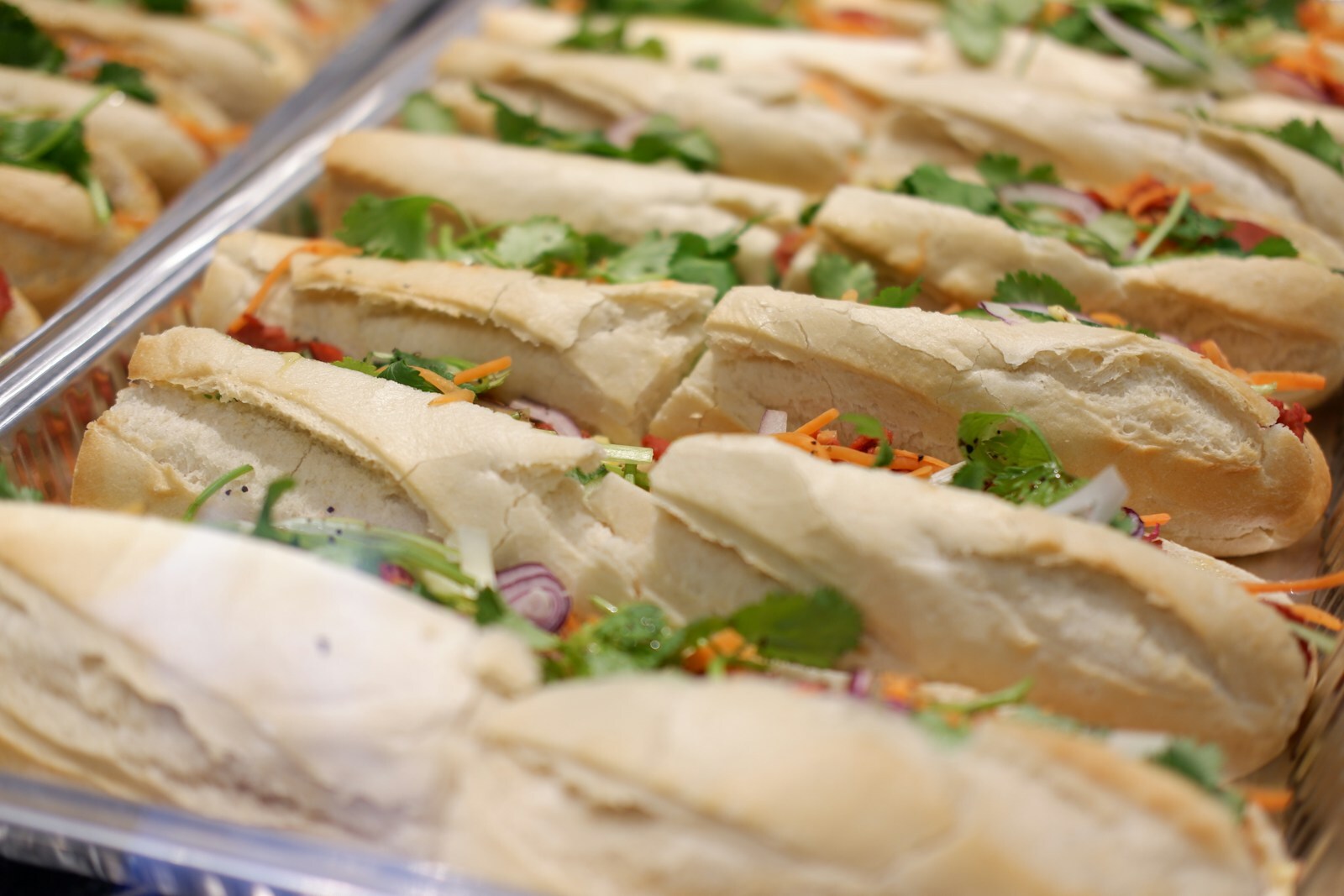 Khay nhôm trắng đầy ổ bánh mì thịt Việt Nam vỏ giòn vàng, nhân thịt rau dưa, chụp cận cảnh từ trên xuống, không có người.